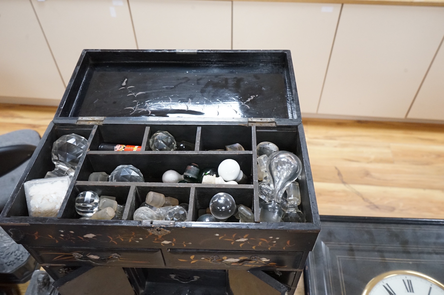 A Japanese lacquer table cabinet with inset porcelain panels, the drawers filled with sundry objects, clay pipes, decanter stoppers, etc, together with a black japanned wall clock, the dial inscribed F. L Hausburg, Paris